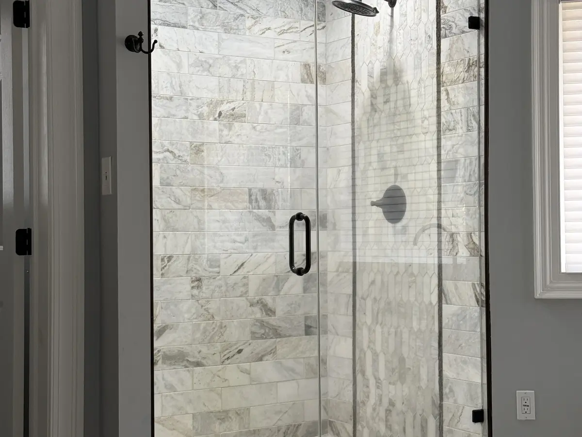 A completed glass-enclosed shower with large-format wall tile and a tiled floor